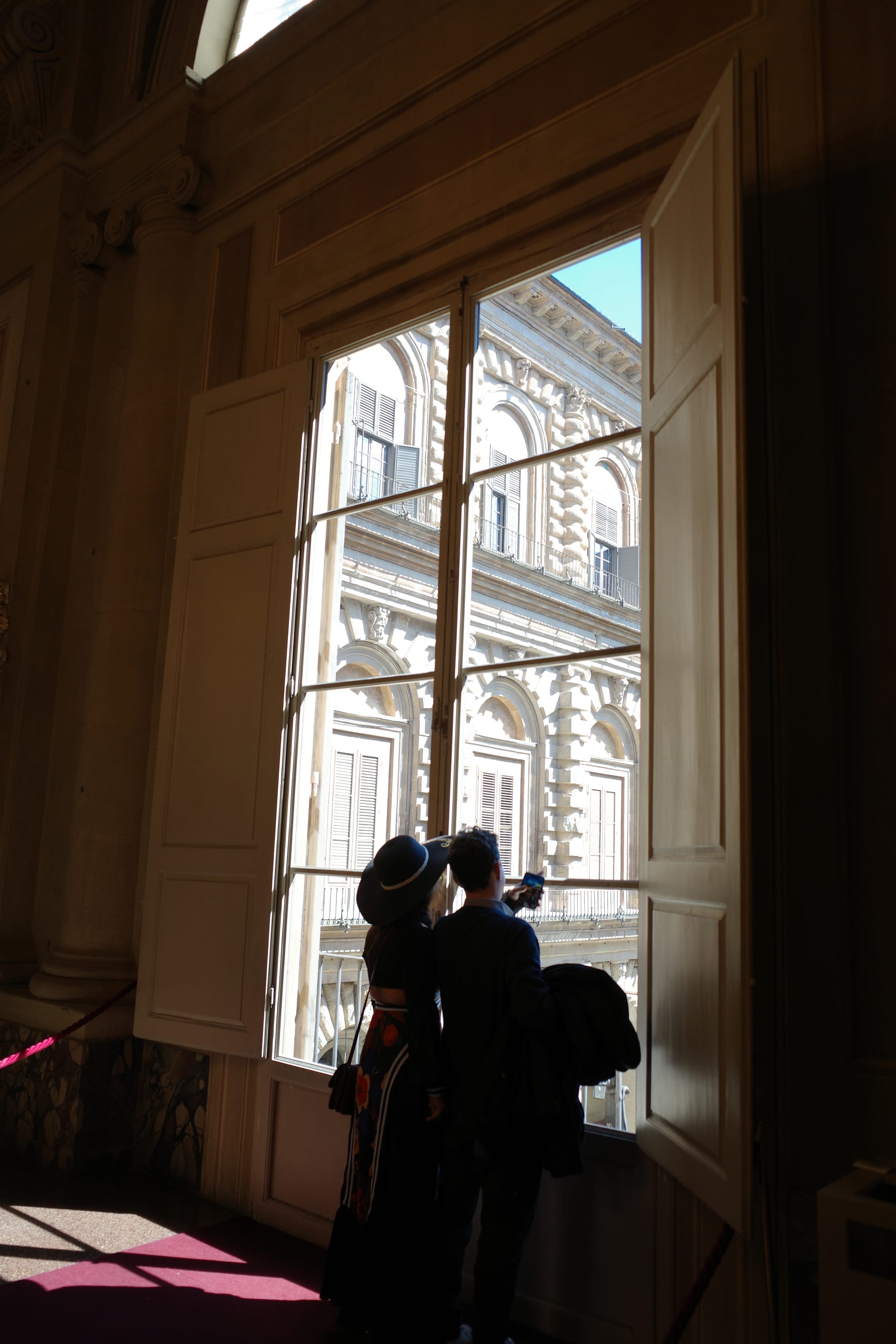 Visitors silhouetted beside a tall window inside Pitti Palace
