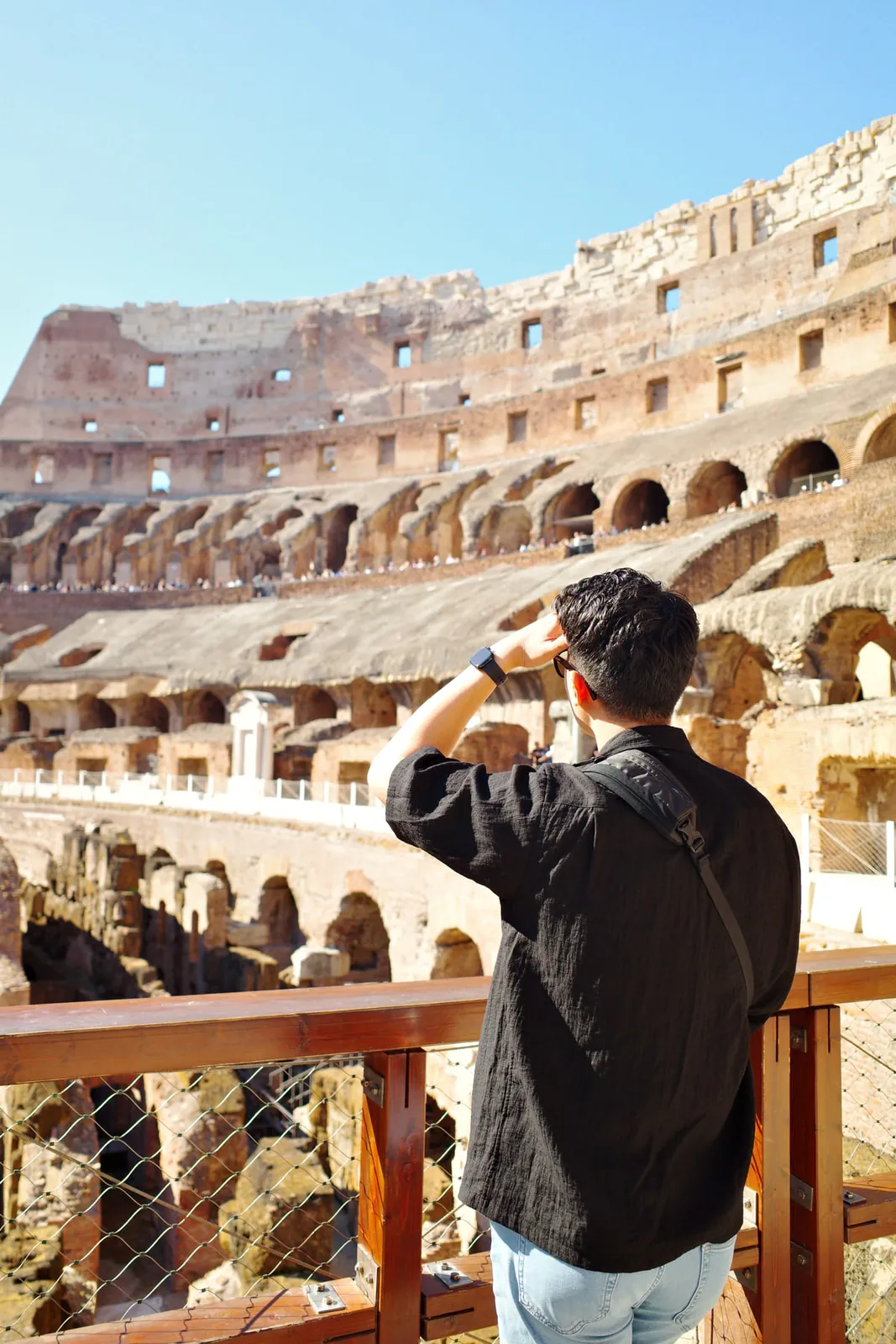 A visitor photographing the Colosseum interior from an upper-level railing
