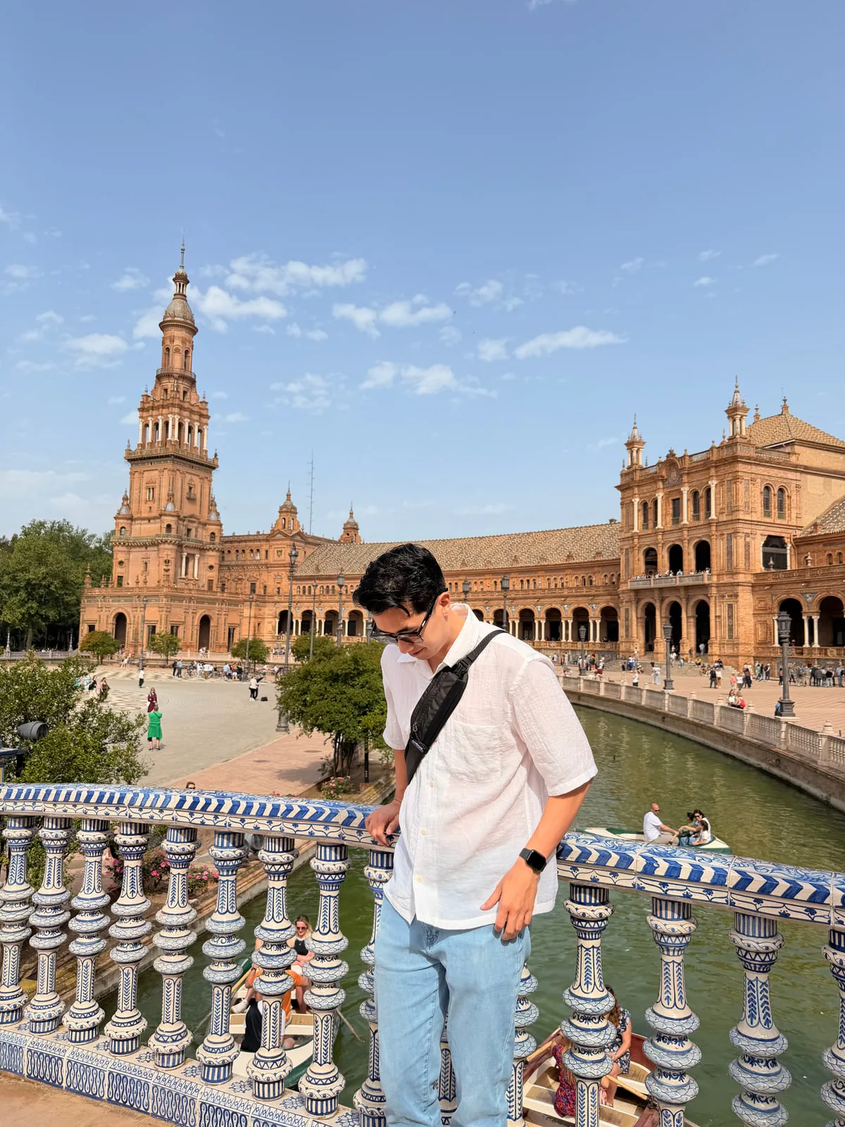 Man standing at the blue-and-white tiled balustrade of a bridge at Plaza de España in Seville