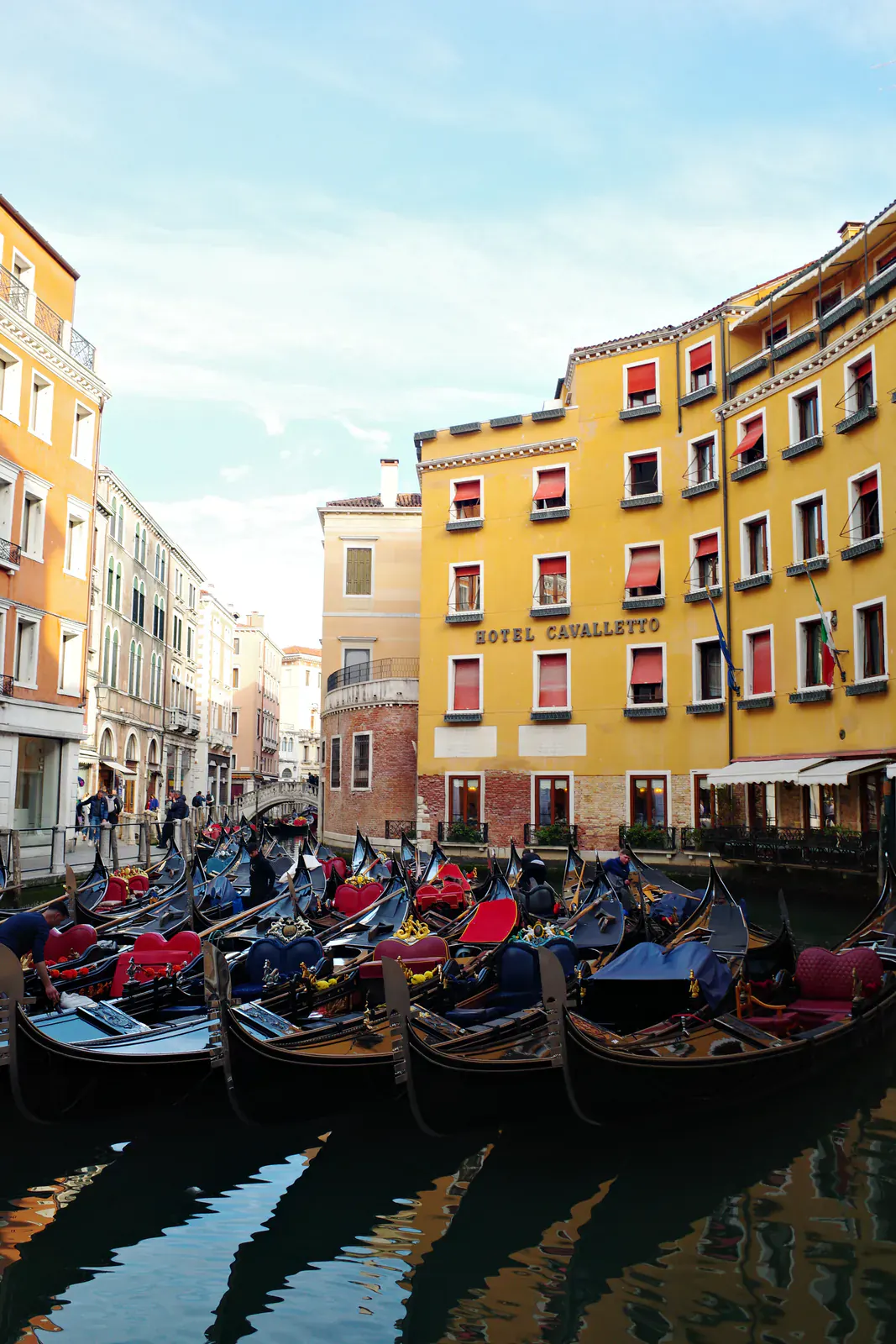 Gondolas moored side by side in a narrow Venetian canal in front of a yellow hotel facade with red awnings
