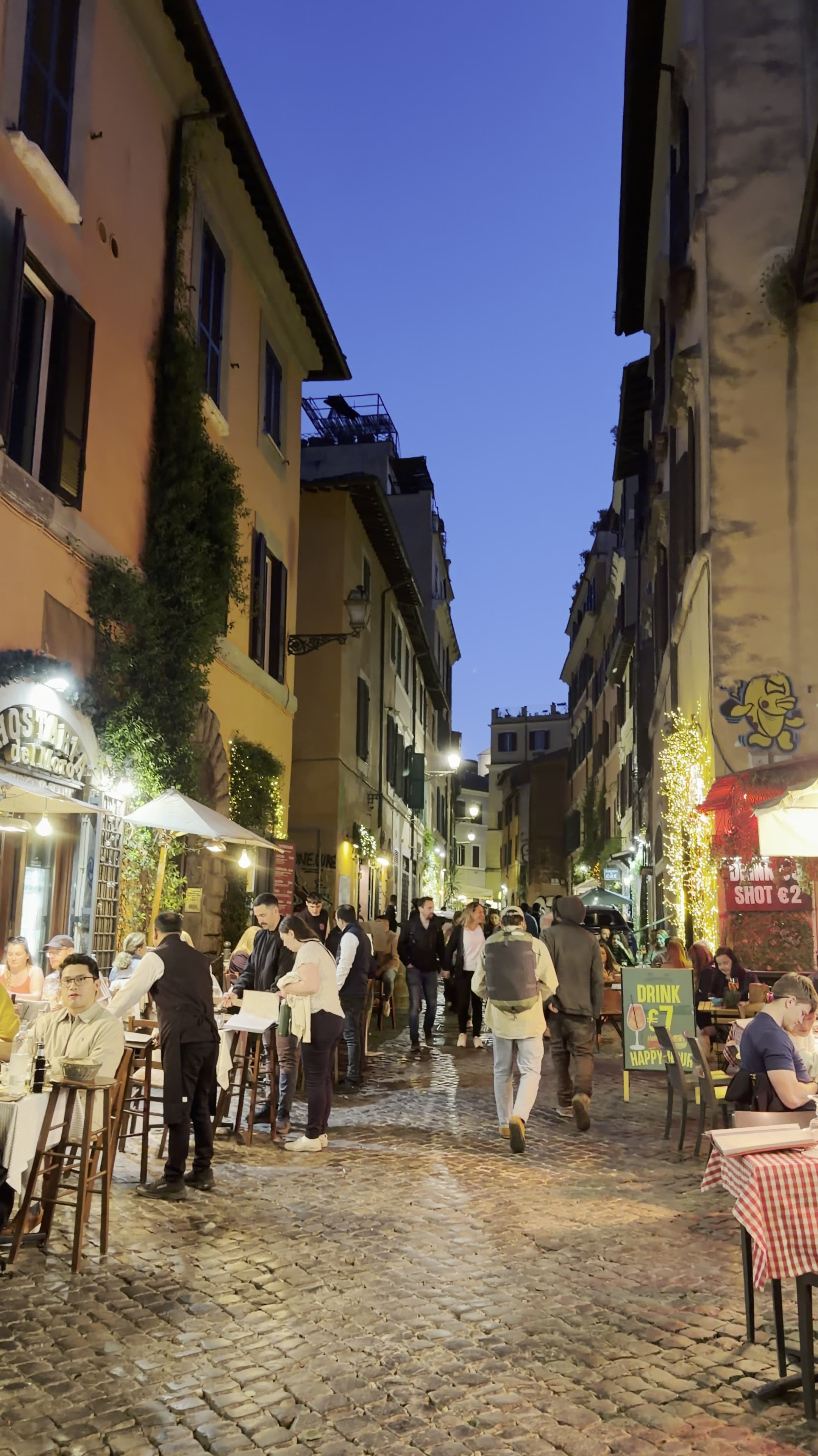 Evening street scene in Trastevere with restaurant tables and warm lights