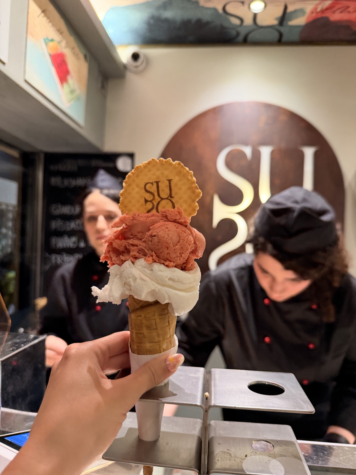 Red and white gelato cone held in front of the Suso logo in Venice